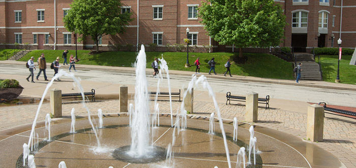 PennWest California students walking behind a flowing fountain.