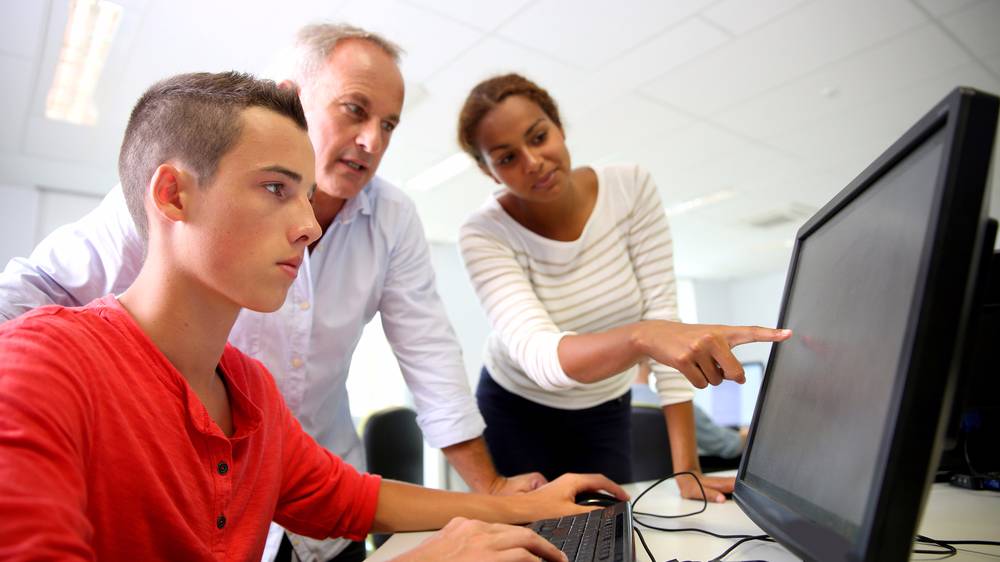 Teachers help a student on a computer.