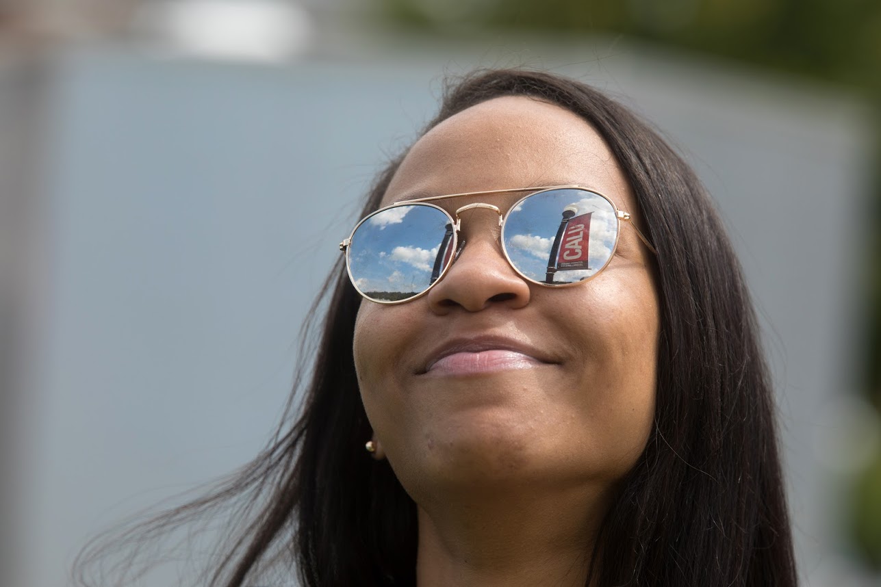 A smiling student wearing sunglasses, with the reflection of a Cal U banner in the lens.